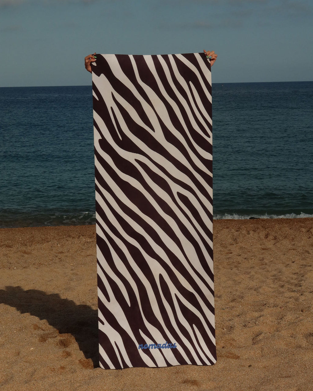 Zebra-patterned yoga mat held up against a beach backdrop with ocean and sky.