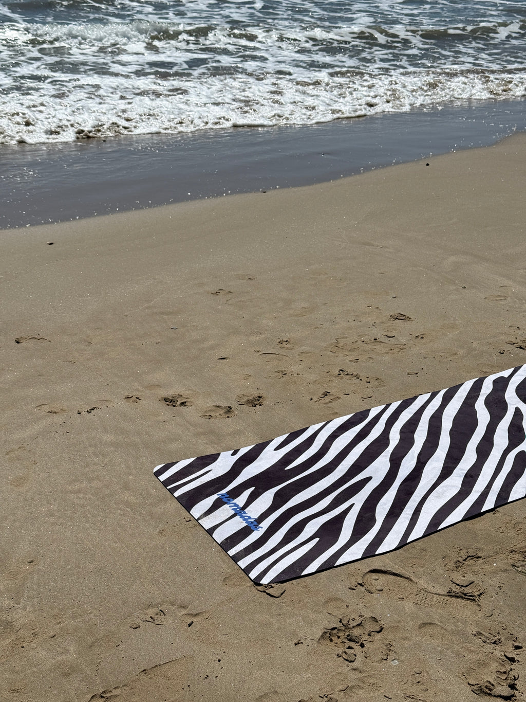Zebra-patterned yoga mat on sandy beach with water in the background