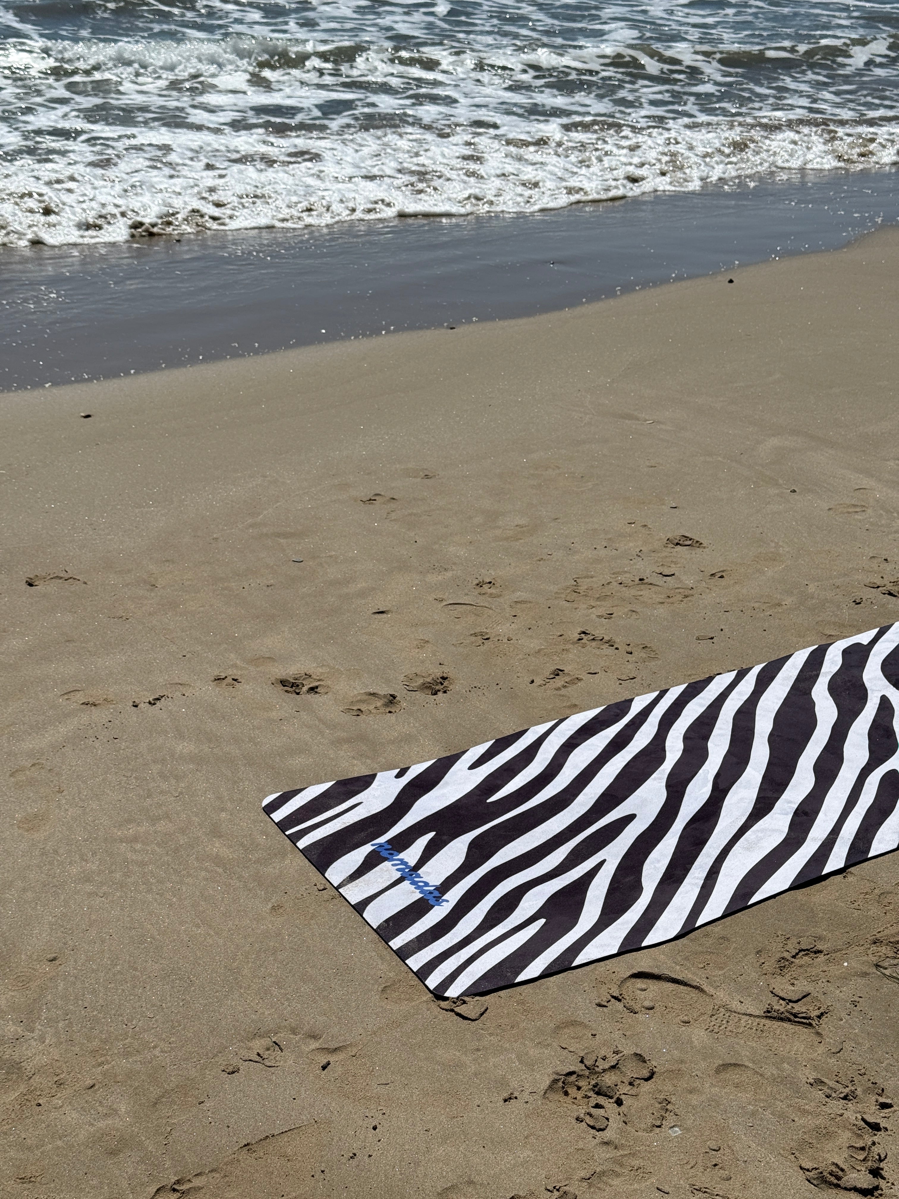 Zebra-patterned yoga mat on sandy beach with water in the background