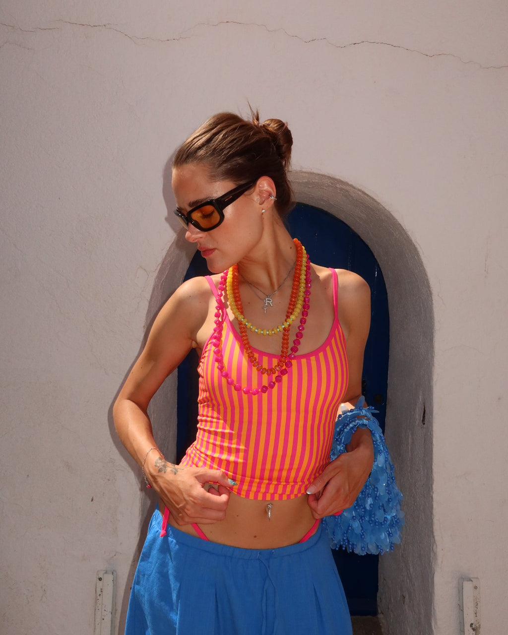 Woman wearing an orange striped tankini top and blue balloon pants standing in a narrow alleyway.