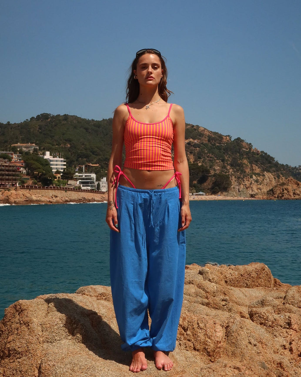 Woman standing on a rocky outcrop by the ocean with a clear blue sky.